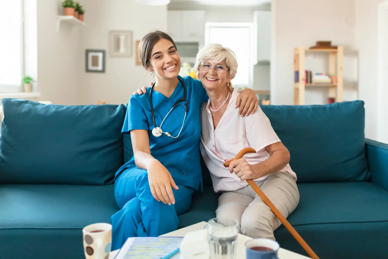 A caregiver and older adult smiling together on a couch at home.